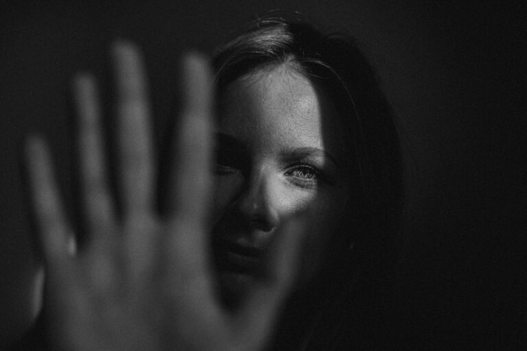 Woman in the shadows holding hand up as if to stop someone