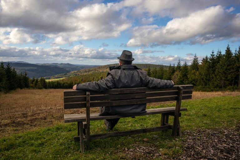 Older man sitting alone on a bench looking out to a beautiful view with dark clouds above