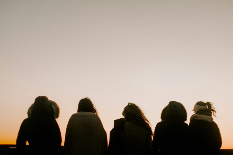 5 people in warm coats sitting on the ground watching the sun go down