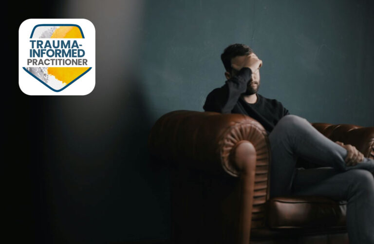 man sits in a dark room on a sofa with his head leaning on his hand with trauma logo