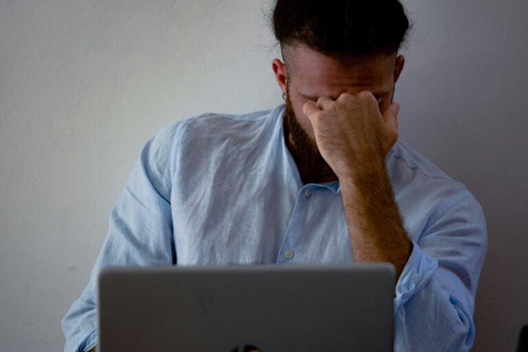 Man in the workplace working at his laptop with his head leaning on his fist looking stressed out
