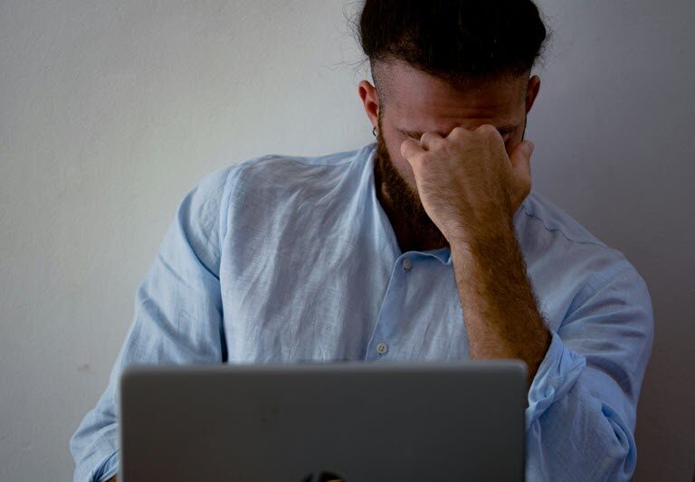 Man in the workplace working at his laptop with his head leaning on his fist looking stressed out